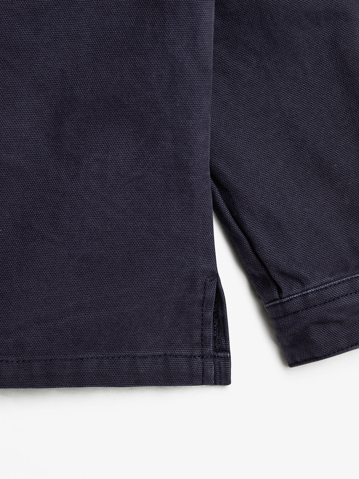 A close-up of a dark blue fabric with visible texture, showing the hem with a side slit detail. The fabric lies flat in a neutral, well-lit setting.