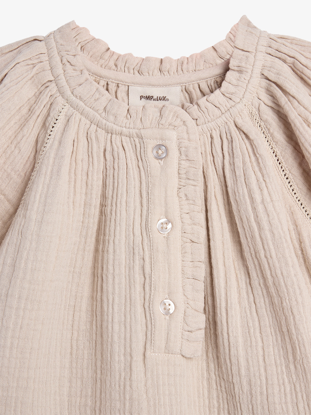 Cream-colored, button-up blouse with ruffled collar and textured fabric. It has a label inside reading "POMPdeLUX." The blouse is laid flat against a plain, light background.