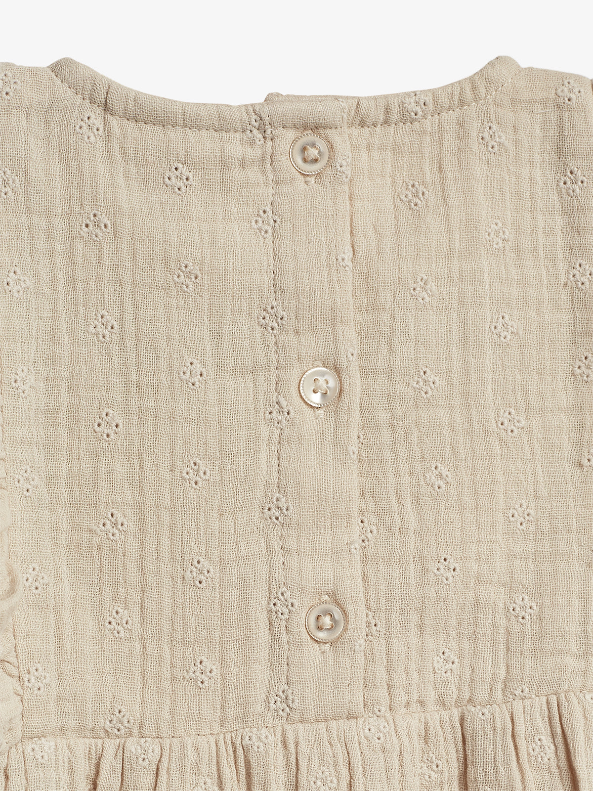 A beige fabric garment with small embroidered floral patterns features a row of three buttons down the back, indicating it might be a dress or blouse in a plain setting.