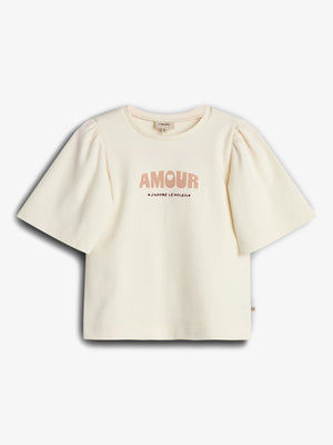 Cream-colored T-shirt featuring puffed sleeves, displays text "AMOUR" and "J’ADORE LE SOLEIL." The shirt is laid flat against a plain white background.