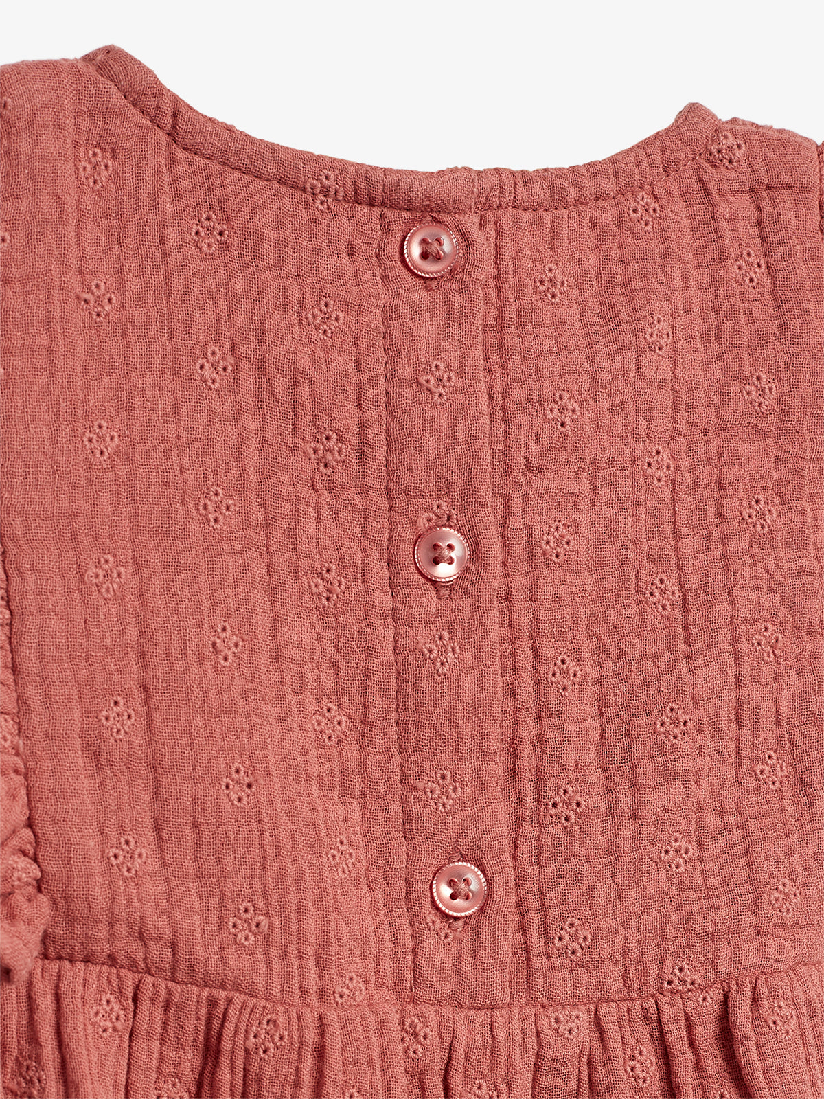 A pink, textured fabric with small floral patterns; three round buttons run vertically down the center. The context is a close-up of a garment's back.