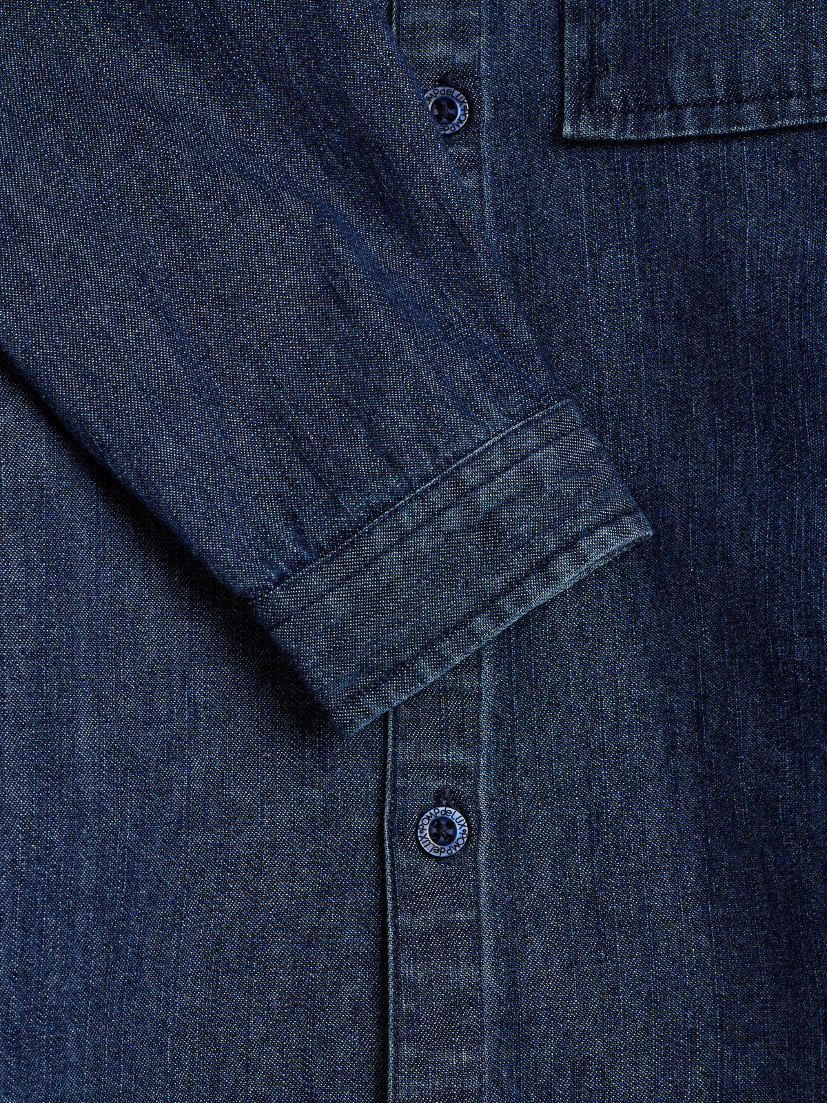 A denim shirt sleeve lays flat, angled diagonally over the button-down section. Visible buttons are detailed with the text "Nordblanc Support Red." The shirt appears unworn, highlighting its dark blue fabric.