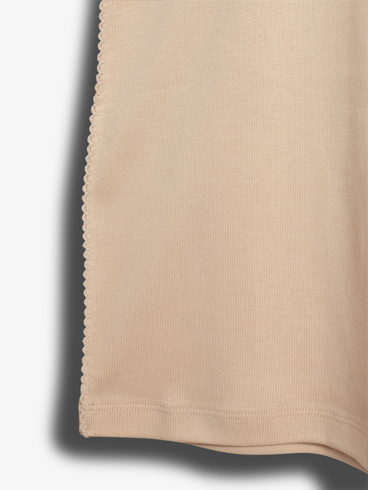 A beige fabric with a scalloped edge hangs vertically, casting a shadow on a plain, light background. The material appears textured, suggesting a soft, stretchy knit.