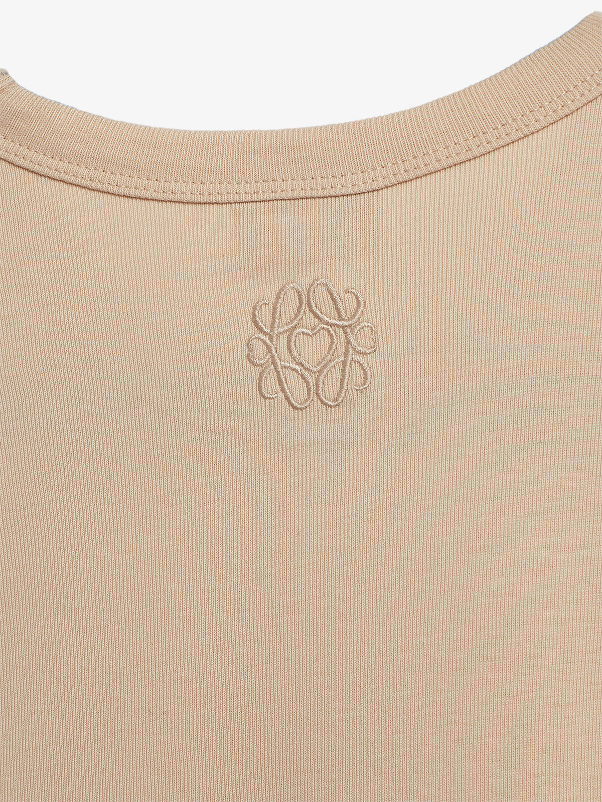 A beige ribbed fabric features a subtly embroidered ornate logo near the neckline, creating a simple yet elegant design.