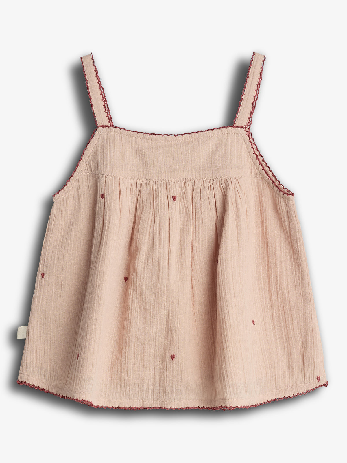Beige sleeveless top with red heart patterns and scalloped red trim. Its lightweight fabric gathers slightly below the bust, and it has slender straps. Set against a plain white background.