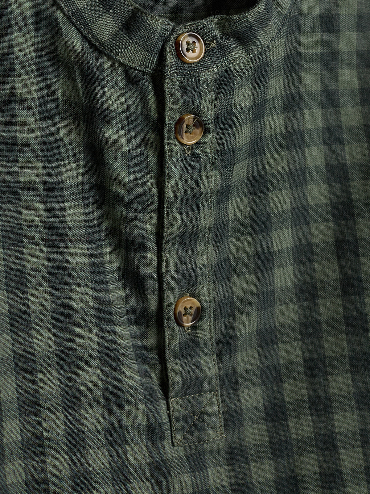 A green and black checkered shirt features buttons along a short placket. The pattern is consistent, creating a casual appearance in the close-up view of the fabric.