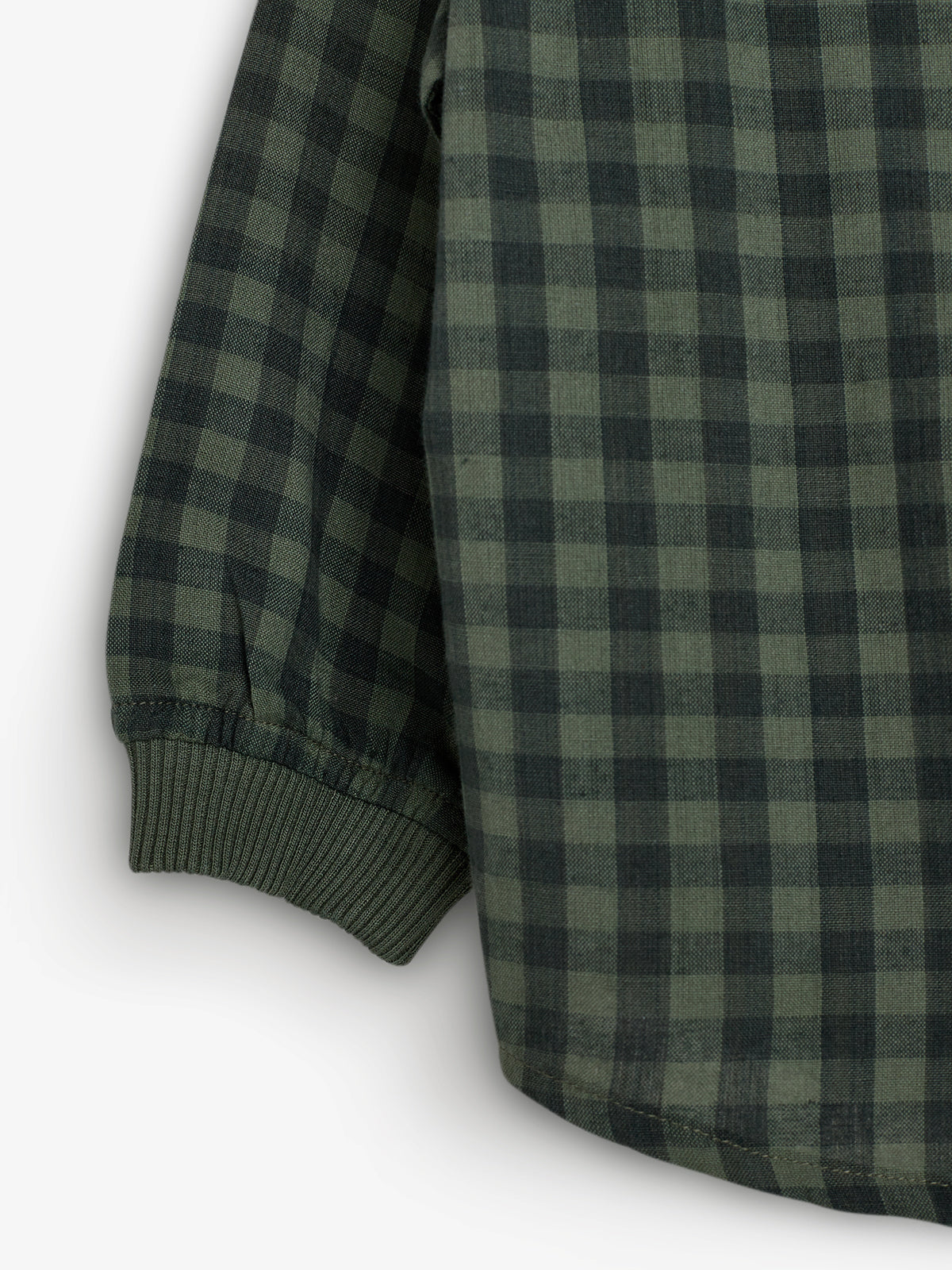 A green checkered fabric forms the sleeve of a garment, with ribbed cuffs. The pattern includes alternating dark and light green squares, suggesting casual or outdoor attire.