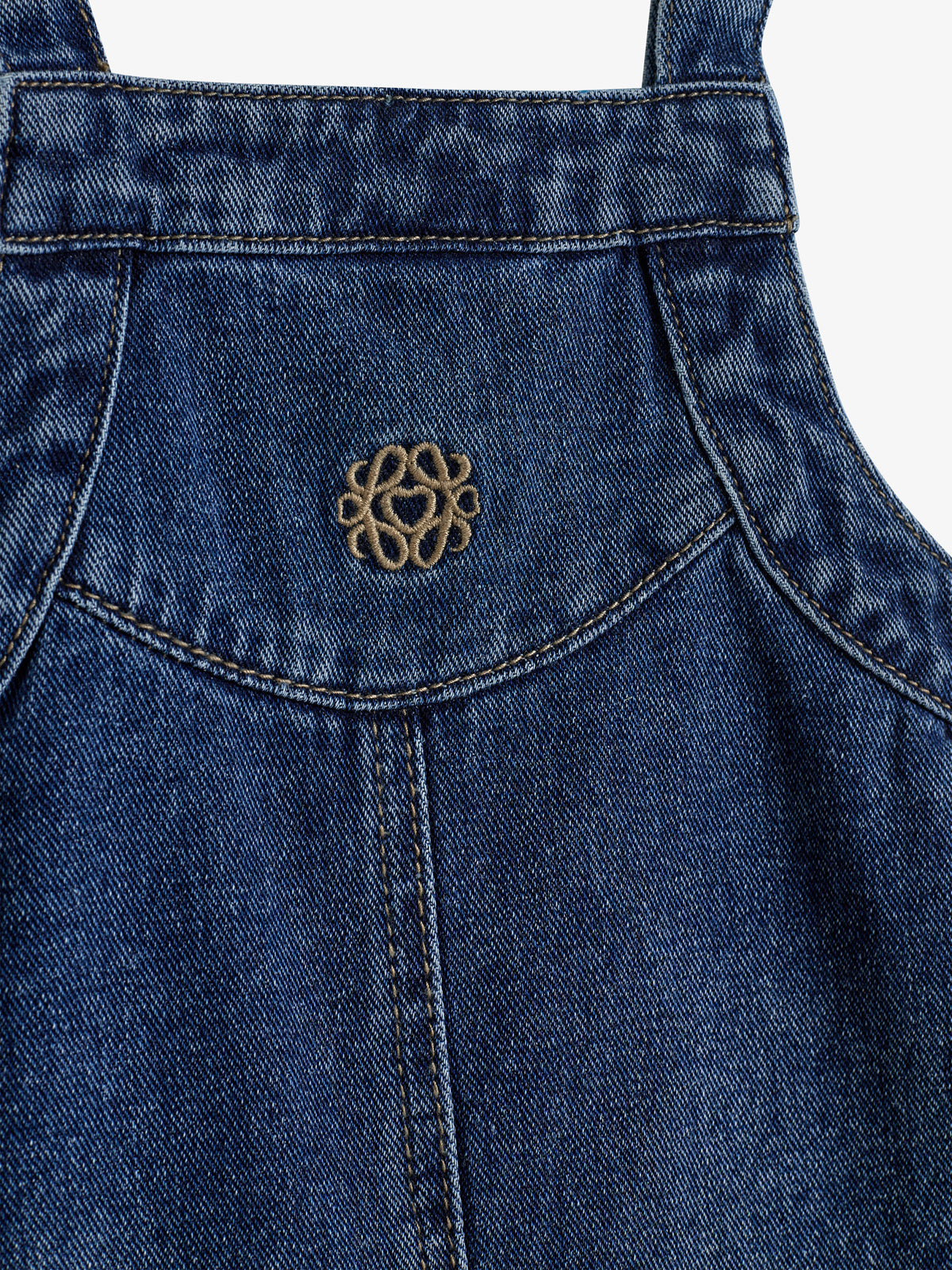 Denim garment features a small embroidered logo, resembling a looped design with a heart, centered on stitched fabric. The background is a plain, neutral setting.