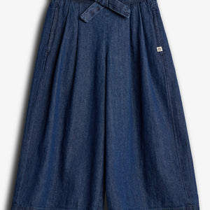 Dark blue denim culottes, featuring a tied waist belt, hang against a plain white background. The wide-legged design includes subtle pleats and a small sewn label on the upper right side.